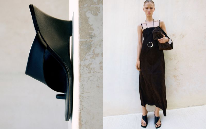 Fashion editorial shot with a woman in a black dress, black handbag and black sandal wedges in an indoor setting against a white wall.
