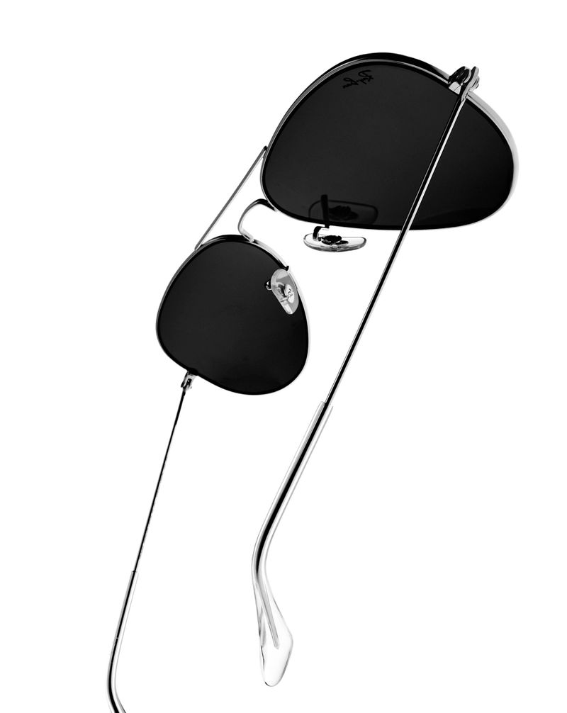 Studio shot of aviator sunglasses with black lenses and silver metal frames against a white backdrop, clean and minimal product photography.