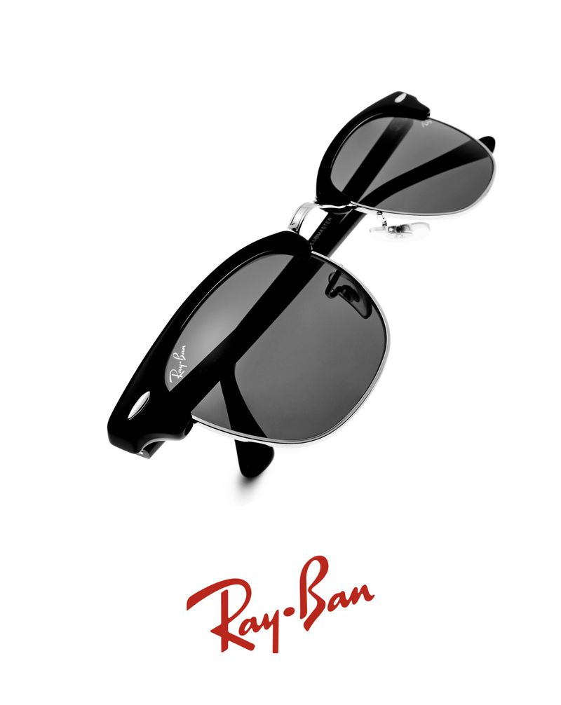 Ray-Ban sunglasses with black frames and dark lenses are angled on a white backdrop, featuring a red Ray-Ban logo.