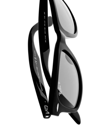 Close-up studio shot of black Ray-Ban Wayfarer sunglasses with grey lenses. The iconic eyewear is set against a stark white background.