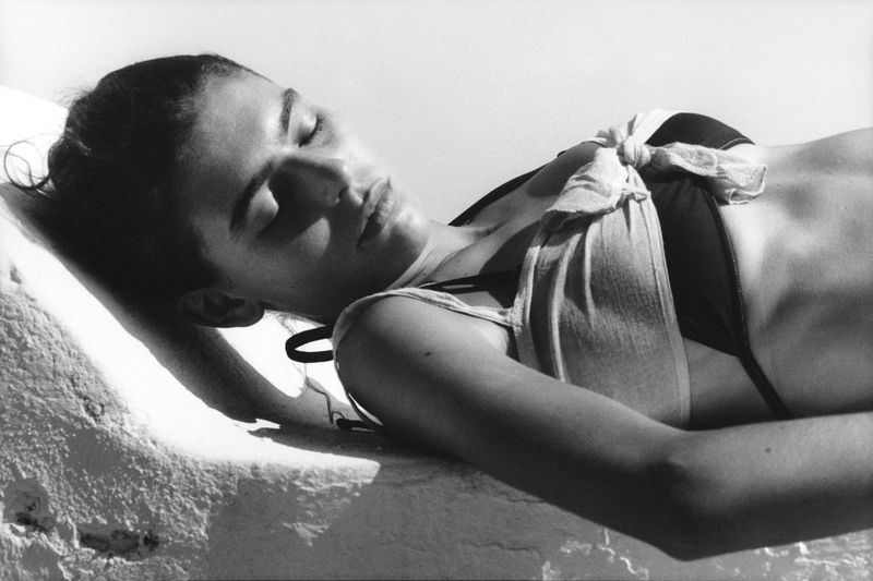 Monochrome image of a young adult woman in swimwear lying in sunlight with her eyes closed, creating a serene and relaxing scene.