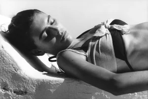 Black and white portrait of a woman reclining outdoors against a bright white architectural surface.
