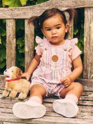 Young child wearing striped overalls seated on a wooden garden bench with a stuffed toy dog