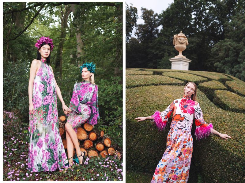 Three fashion models wearing colorful floral dresses and flower headbands pose in an outdoor garden and forest setting.