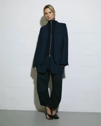 Model Camilla Deterre wearing a navy blazer and trousers for Roucha Spring 24 against a white wall.
