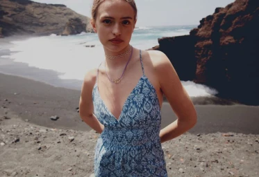 Woman in patterned blue dress on a dark sandy beach with ocean waves in background for Mango vacation scene campaign