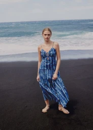 Model wearing a blue tie-dye maxi dress on a dark sandy beach by the ocean for Mango Vacation Scene