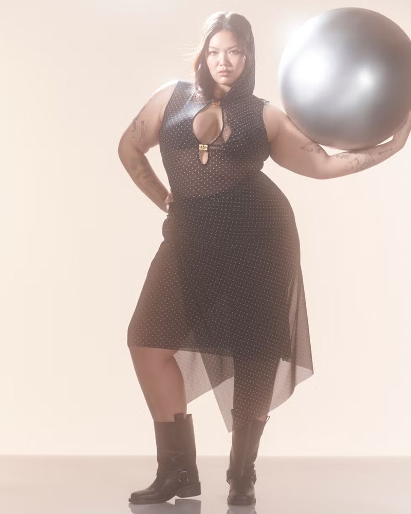 Adult woman in a hooded polka dot outfit poses with a fitness ball in a studio setting, looking directly at the camera. 