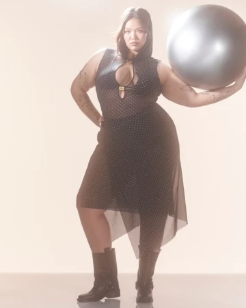 Adult woman in a hooded polka dot outfit poses with a fitness ball in a studio setting, looking directly at the camera. 