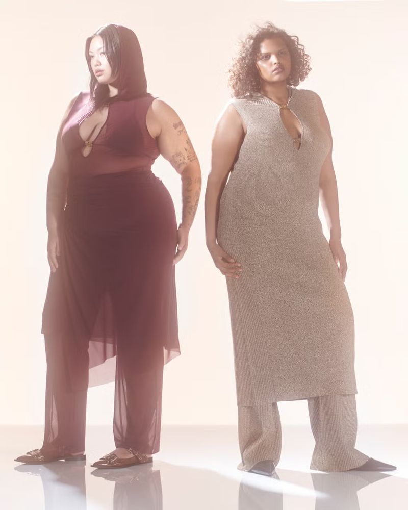 Two plus-size women pose in a photo studio wearing stylish sleeveless pantsuits in a fashion editorial, showcasing their curvy figures.