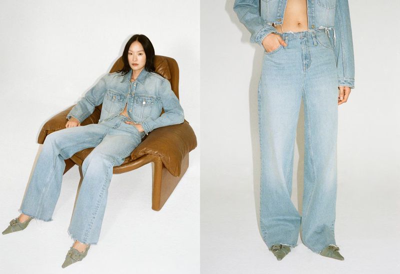 A woman sits in a brown leather chair, wearing a light blue denim jacket and flared jeans against a white backdrop in a fashion shoot.
