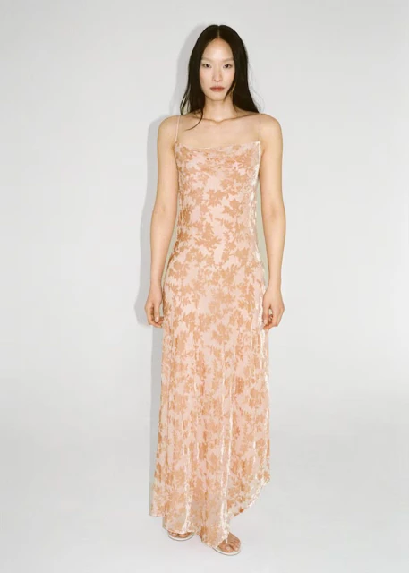 Full shot of a slender Asian woman posing in a long dress with a floral pattern against a bright white background in a studio setting.