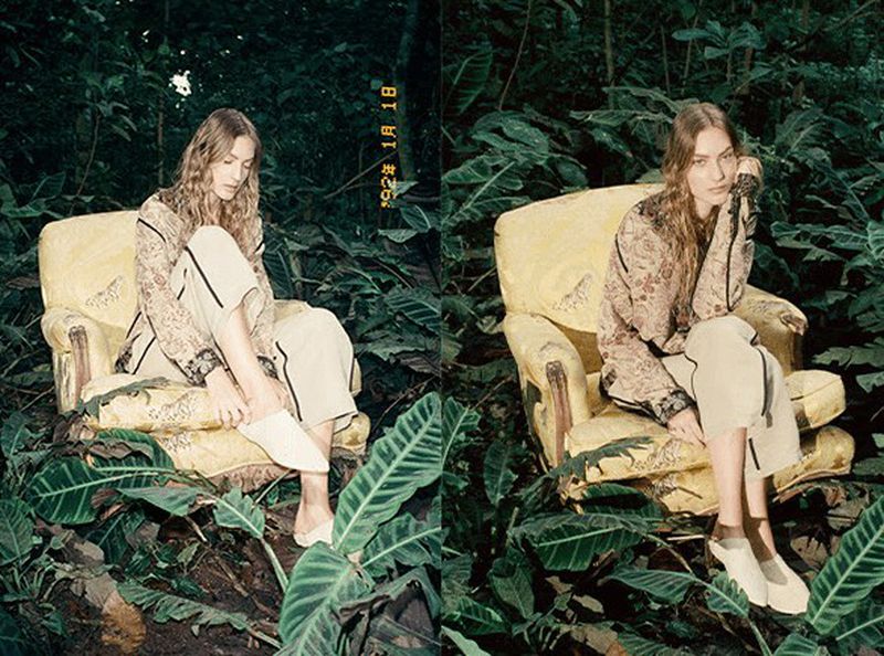 A woman with long blond hair sits in a yellow armchair, surrounded by green foliage. She wears a floral shirt and beige pants.