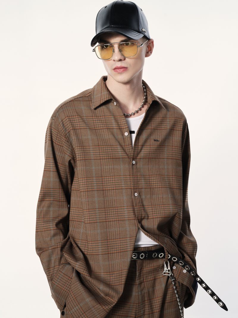 Studio shot of a young adult male wearing a brown plaid patterned shirt and matching pants, paired with a black leather baseball cap.