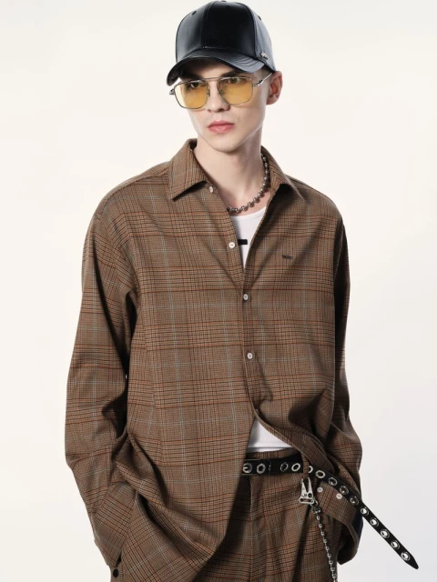Studio shot of a young adult male wearing a brown plaid patterned shirt and matching pants, paired with a black leather baseball cap.