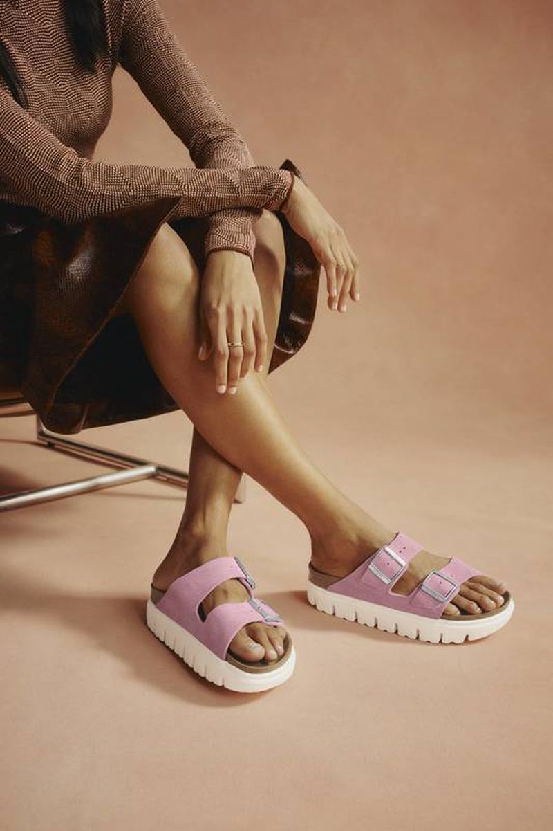 Woman sitting and posing in pink platform sandals against a pink background, highlighting fashion and footwear.