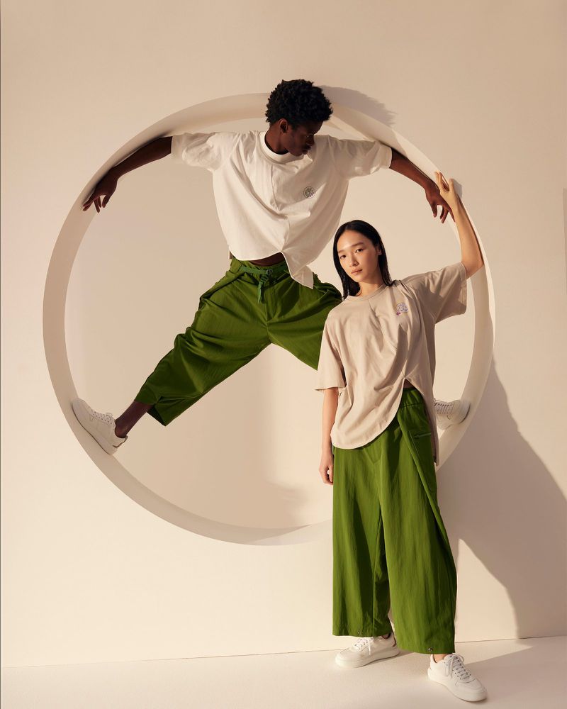 Two people pose in a circle frame, showcasing fashion apparel. One is jumping in the circle and the other is standing in front of it.