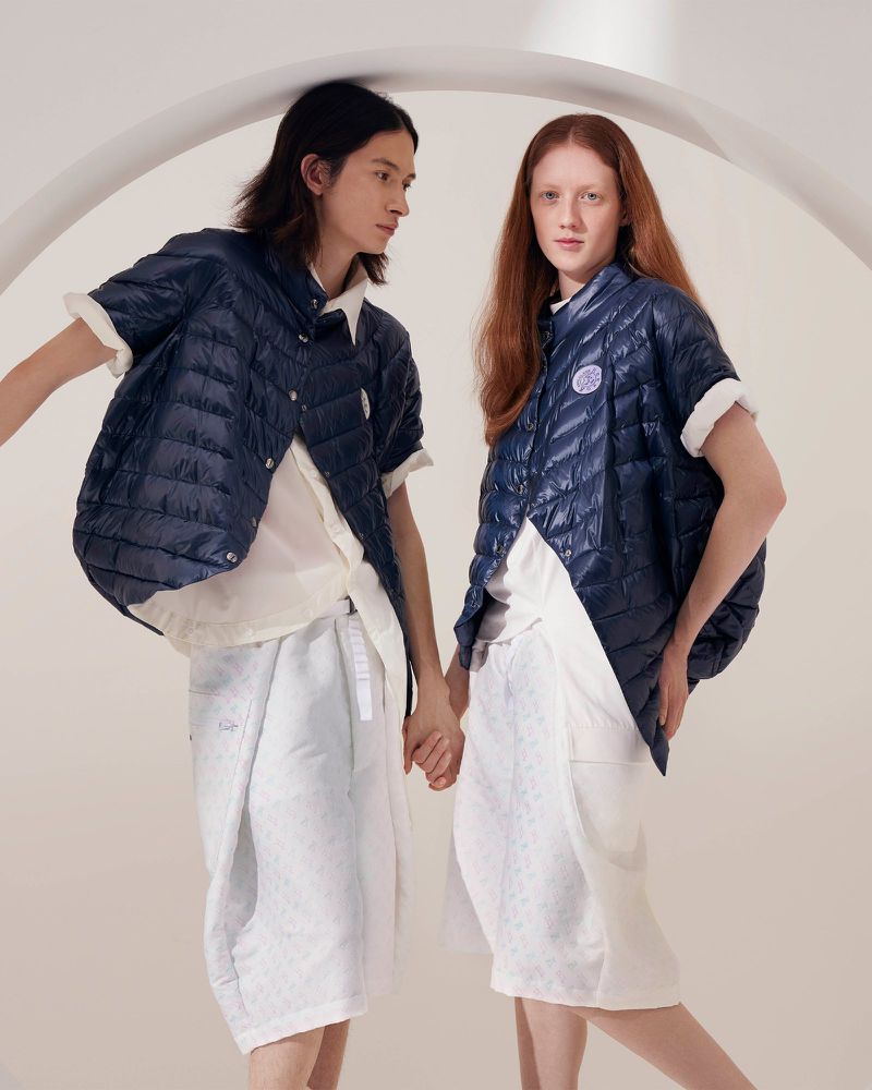 Two models in a photo studio showcase navy blue quilted vests and patterned white shorts, presenting a fashionable and modern apparel collection.