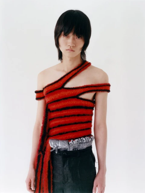 Portrait of a person with dark hair wearing a red and black striped top, posing against a plain white backdrop in a studio setting.
