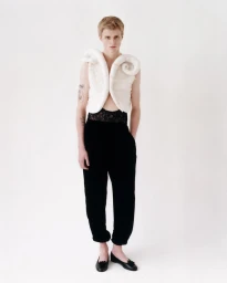 Model wearing a white sculptural vest and black trousers against a plain light background for Transe Paris lookbook.