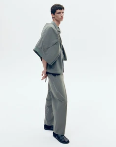 A male model wearing a grey technical jacket and trousers with black shoes against a plain white background.