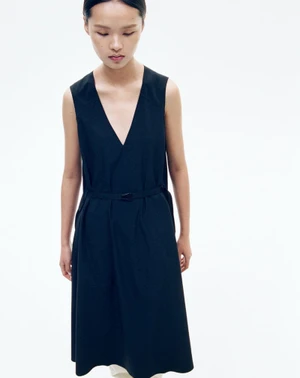 Model wearing a black sleeveless v-neck midi dress against a plain white studio background