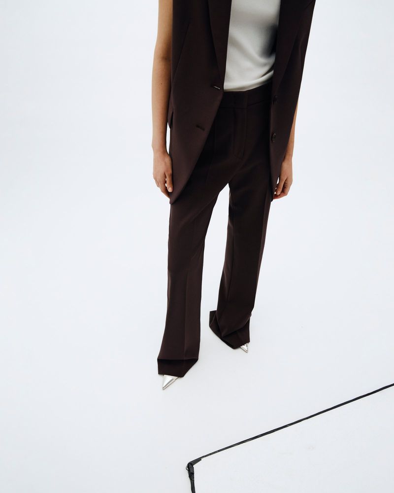 Fashionable brown vest and trousers outfit. Woman posing in a sleeveless blazer with matching pants, metallic pointed toe heeled shoes.