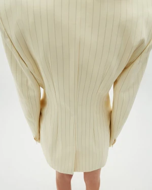Model from behind wearing a cream pinstripe blazer against a white seamless backdrop