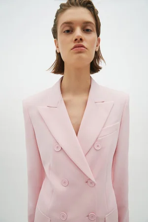 Model wearing a pale pink double-breasted blazer against a clean white studio backdrop.