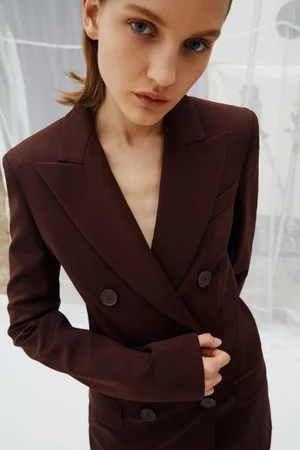Model wearing a structured dark brown double-breasted blazer against a white translucent backdrop