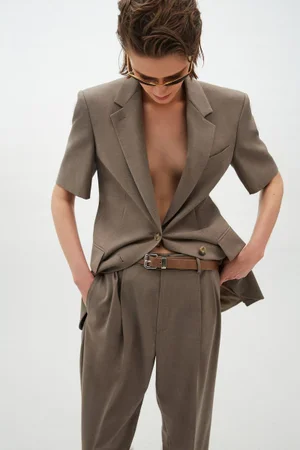Model wearing a brown short-sleeve blazer and trousers with a belt against a white backdrop