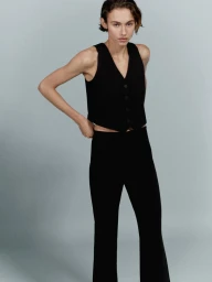 Model wearing a black vest and trousers against a neutral grey studio backdrop