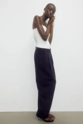 Model wearing a white top and dark trousers posing against a plain white studio background.