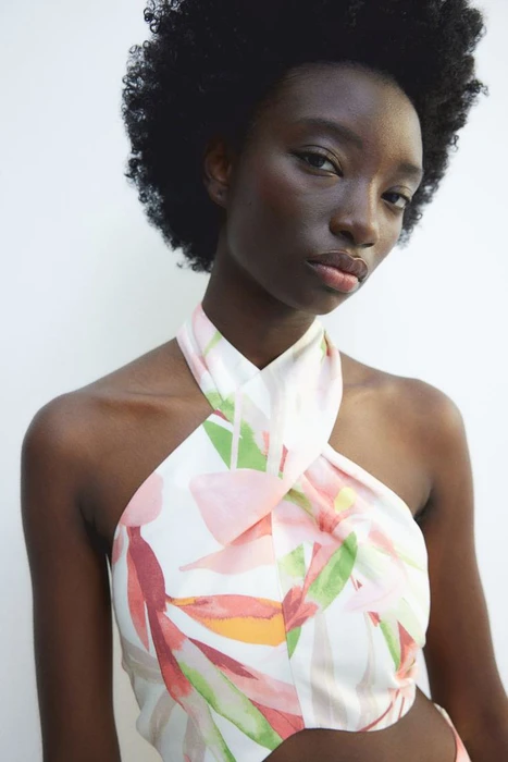 Portrait of a Black woman wearing a floral print halter neck dress against a white background for H and M