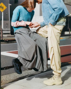 Two models outdoors leaning against a black metal railing, wearing layered casual apparel and sneakers.