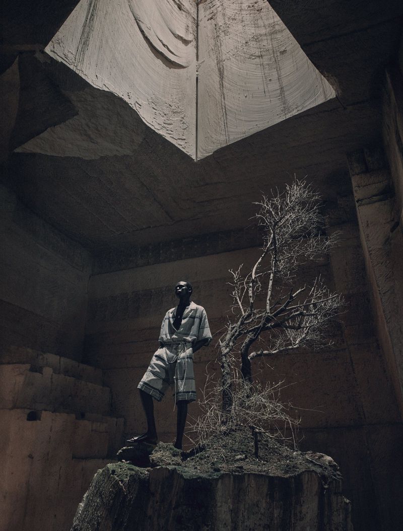 Fashion shot in a quarry featuring a Black male model in patterned shorts and top, standing on a rock with a bare tree.