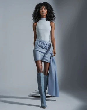 Model wearing a light blue sleeveless top, draped skirt, and matching knee-high boots against a grey studio backdrop.