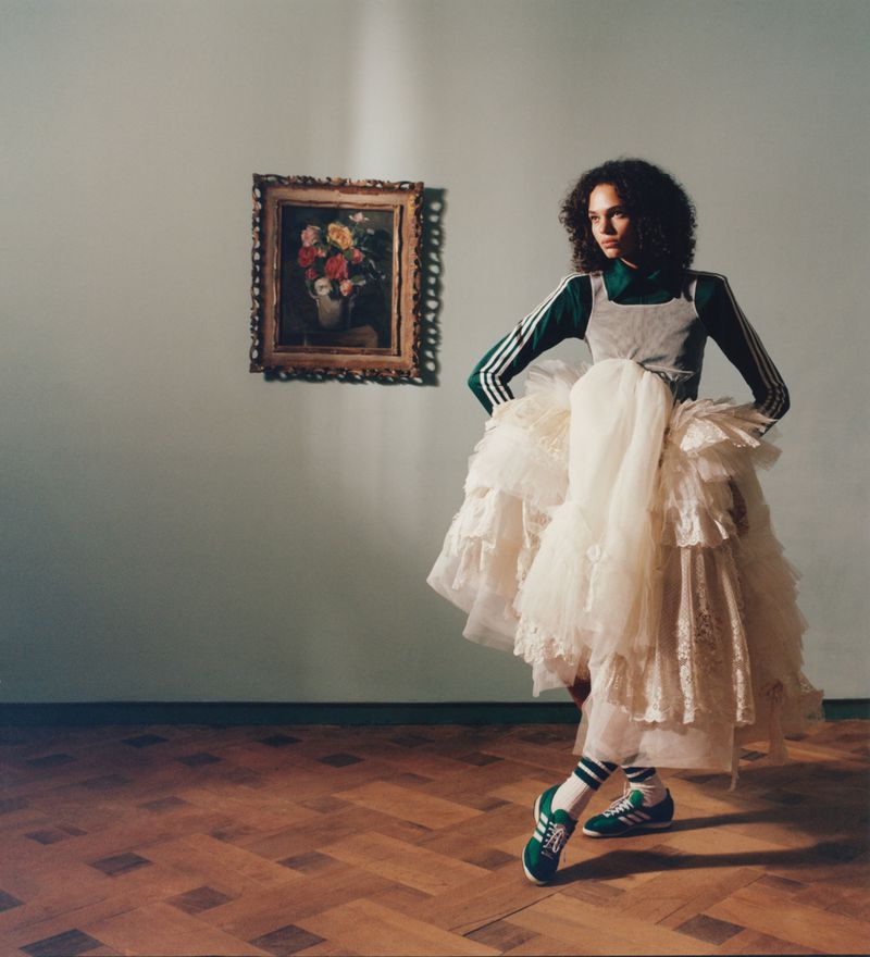 Elegant woman posing in a green athletic top and sneakers paired with a voluminous white ruffled dress, art gallery backdrop, for fashion.