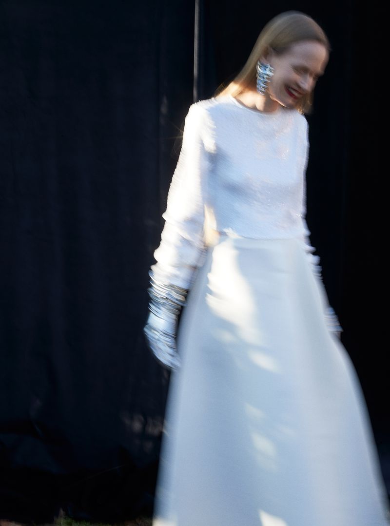 Model in a white long-sleeve dress and statement earrings captured with motion blur against a dark backdrop.