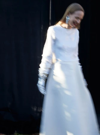 Model in a white long-sleeve dress and statement earrings captured with motion blur against a dark backdrop.