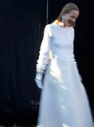 Model in a white long-sleeve dress and statement earrings captured with motion blur against a dark backdrop.