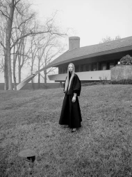 Model standing on a grassy slope in front of a modern house for Maison Cogo FW2425
