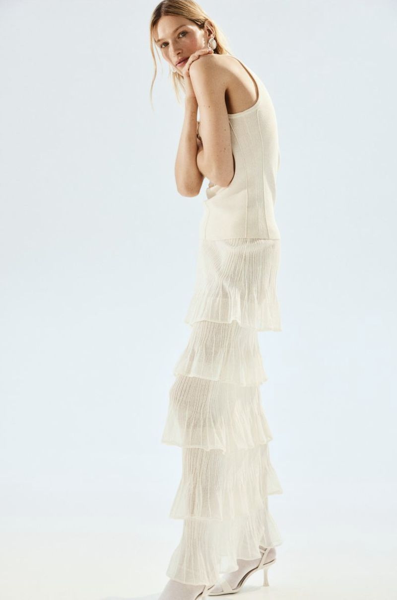 Model Liz Kennedy wearing an off-white tank top and tiered pleated ruffle maxi skirt against a pale studio background.