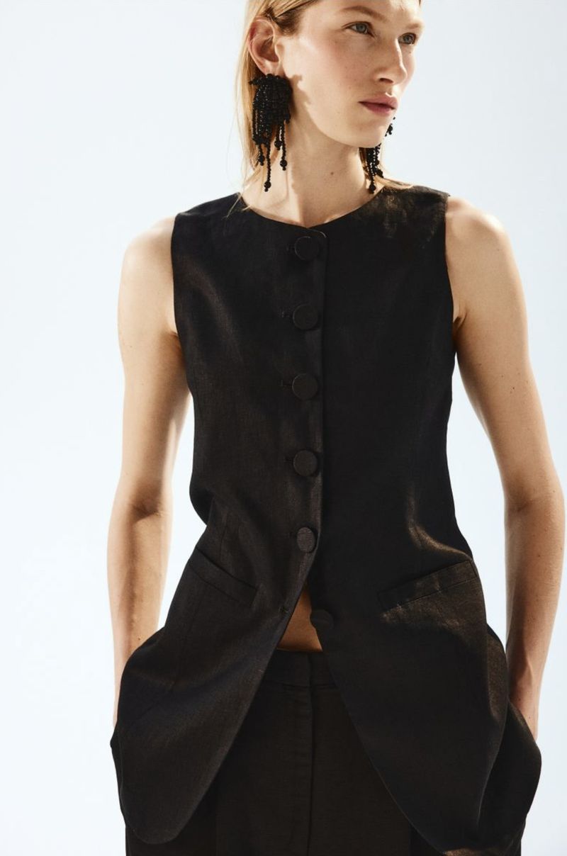 Elegant woman in sleeveless black top and matching trousers. Close-up shot, fashion-forward style against a bright white backdrop.