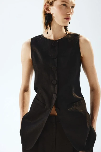 Elegant woman in sleeveless black top and matching trousers. Close-up shot, fashion-forward style against a bright white backdrop.
