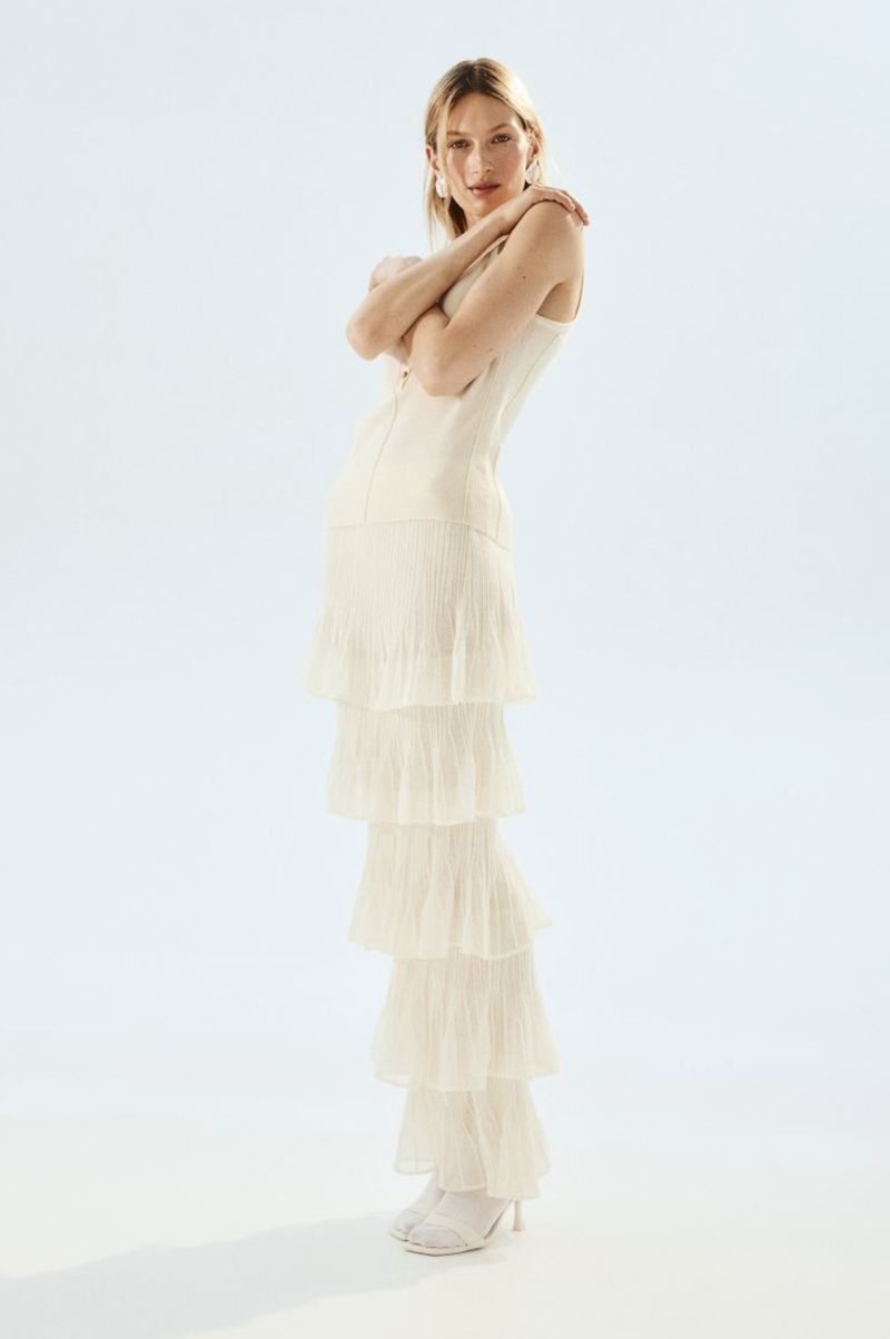 Model Liz Kennedy wearing a tiered cream sleeveless dress against a white background for H&M EDITION Collection Petals