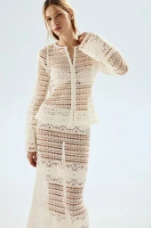 Model Liz Kennedy wears an off-white lace knit cardigan and matching skirt against a bright seamless studio background.