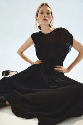 Model Liz Kennedy wearing a black pleated dress and oversized silver earrings against a white backdrop.
