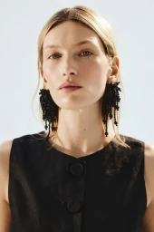 Model Liz Kennedy wearing beaded black earrings and a sleeveless black top against a clear sky background for H&M.