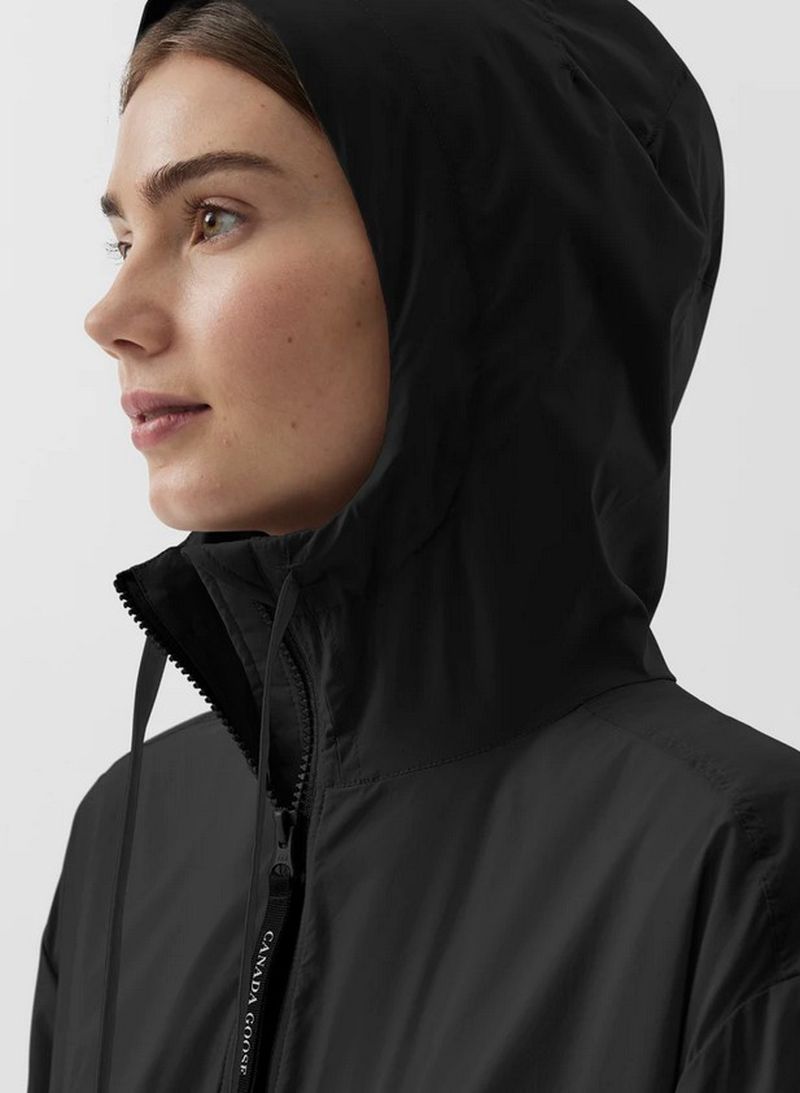 Close-up of an adult female wearing a black hooded jacket, featuring a zip-up closure, side profile, and neutral facial expression.